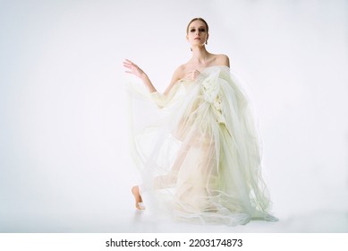 A Young Girl Model In A Photo Studio In A Wedding Dress Sitting On One Knee Playing With A Dress