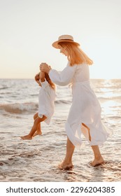 A young girl, mother, with a little daughter in white dresses, walk on the water on the seashore at sunset. The sun breaks through your hair - Shutterstock ID 2296204385