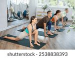 Young girl with multinational group of active people doing stretching exercises during yoga class in sports club