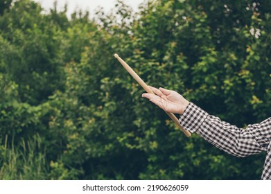 Young  Girl Musician Drummer In Plaid Shirt, Her Hand Twirling Drumstick With Virtuosity Against Dark Greenery Of Garden