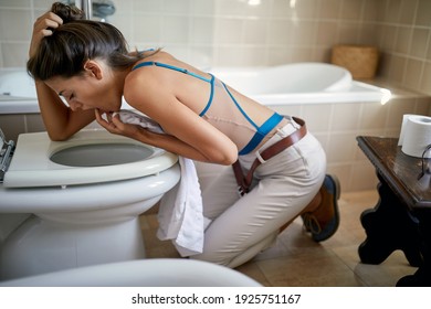 A young girl with nausea is kneeling on the floor and forcing herself on vomit in the toilet. Bathroom, toilet, nausea, morning