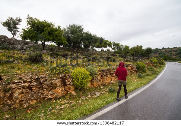 A young girl next to a road in the\
mediterranean in rainy weather with hood on her\
head