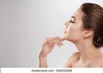 Young Girl With Nude Make Up And Naked Shoulders Posing At Grey Background, Beauty Photo Concept, Skin Care, Hydrated Skin, Portrait, Close Up.