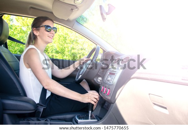 young girl in office clothes and\
sunglasses driving car, view in the cab with bright\
sunlight