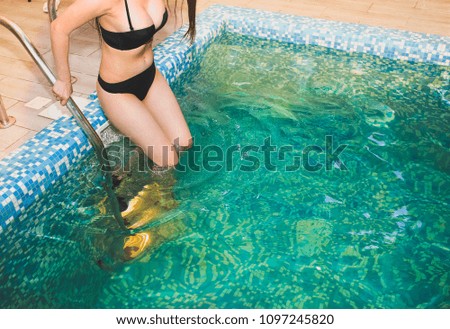 Young girl on black bikini is swimming in the blue pool at the fitness centre. Woman is relaxing after a hard day. Healthy living lifestyle concept.