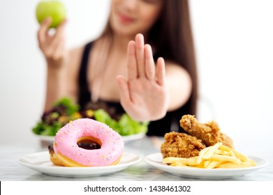 Young Girl On Dieting For Good Health Concept. Close Up Female Using Hand Reject Junk Food By Pushing Out Her Favorite Sweet Donuts And Fried Chicken And Choose Green Apple And Salad For Good Health.