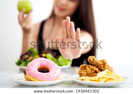 Young girl on dieting for good health concept. Close up female using hand reject junk food by pushing out her favorite sweet donuts and fried chicken and choose green apple and salad for good health.