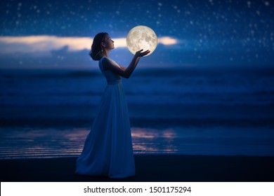 A young girl on a night beach holds the moon, with a starry sky. Art photography