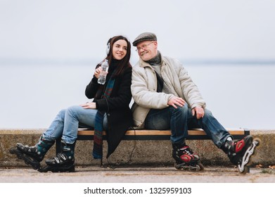 A young girl on roller skates and her father of retirement age are sitting on a bench and smiling at each other. Water and sport. The concept of strong family relationships.