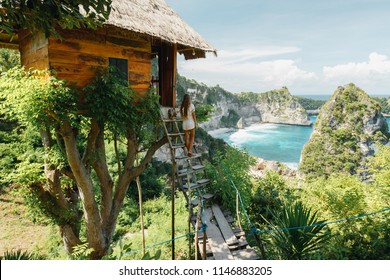 Young girl on steps of traditional house on tree, look at Atun beach, Nusa Penida island. Popular travel destination on Bali holidays. Indonesian background.  travel lifestyle concept