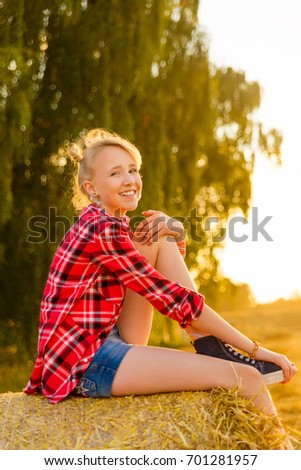 Young girl on straw sheaves in a field. Girl on a wheat field in the rays of the setting sun.
