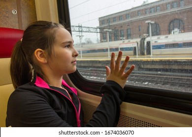 Young Girl On A Train Getting Ready For A Trip. Girl Smiling At Camera With Her Back To A Window On A Cloudy, Cold Day At A Train Station.