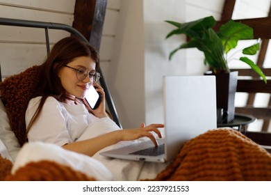 A young girl orders food delivery home late in the evening on the Internet, rests with a laptop in bed, laziness. - Shutterstock ID 2237921553
