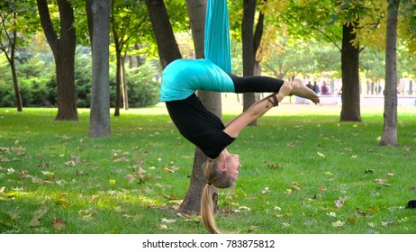 A young girl in a park engaged in aerial yoga. This type of yoga on special fabric canvases