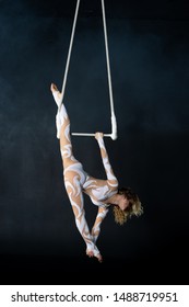A young girl performs the acrobatic elements in the air trapeze. Studio shooting performances on a black background