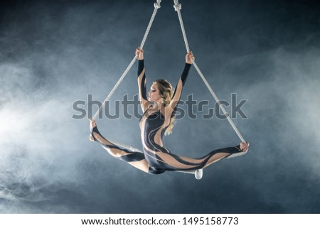 A young girl performs the acrobatic elements in the air trapeze. Studio shooting performances on a black background