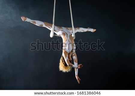 A young girl performs the acrobatic elements in the air trapeze. Studio shooting performances on a black background