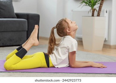 Young girl performs complex yoga stretch, raising her foot towards her head on purple mat, showing flexibility and skill. - Powered by Shutterstock