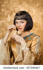 Young Girl With Perfume Bottle. Glamorous Closeup Portrait Of Beautiful Sexy Stylish Brunette Young Woman Model With Bright Makeup With Gold Jewelery. Cleopatra