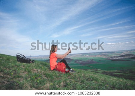 Young girl is photographed on cellphone on a hill in the countryside.