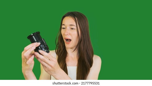 young girl photographer holds a lens in her hands, puts forward the optics and is surprised at the increased size. Chroma key, green screen, portait, close-up.