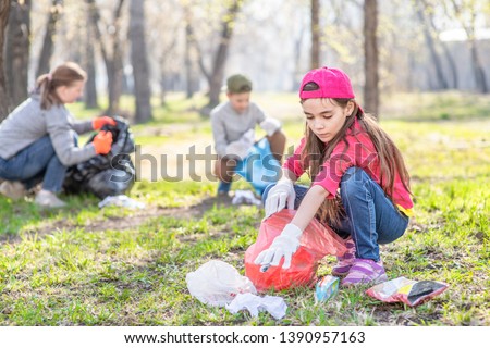 Young girl picking up trash in the park. Volunteer concept