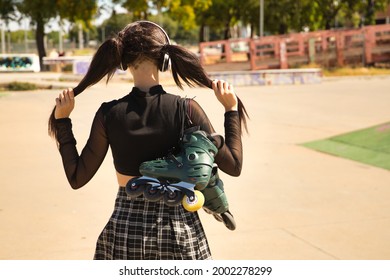 Young girl with pigtails, punk style, white headphones and inline skates hanging from the shoulder of her back holding the pigtails with her hands.