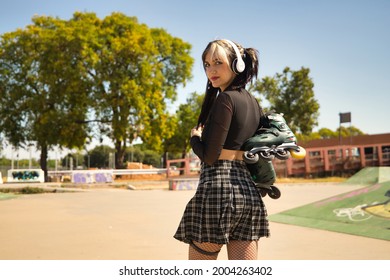 Young girl with pigtails, punk style, white headphones and inline skates hanging from the shoulder on their backs looking at the camera.