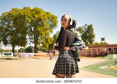 Young girl with pigtails, punk style, white headphones and inline skates hanging from the shoulder on their backs looking at defiant camera.