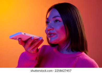 Young girl in pink sweater recording voice message and phone over gradient orange background in neon light  Concept emotions  facial expression  youth  lifestyle  inspiration  sales  ad