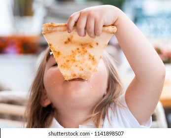 A young girl with plaits is eating a piece of pizza