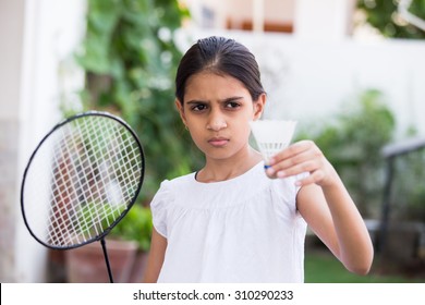 young girl playing badminton outdoors holding a racket and a shuttle cock in a pose to serve