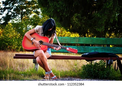 Young Girl Playing Guitar On A Bench Outside.