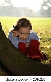 Young girl playing hide and seek holding a mobile phone