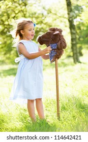 Young Girl Playing With Hobby Horse In Summer Field