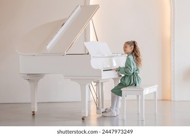 A young girl is playing the piano. She is wearing a green dress and has her hair in a ponytail - Powered by Shutterstock