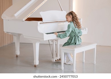 A young girl is playing the piano. She is wearing a green dress and has her hair in a ponytail - Powered by Shutterstock