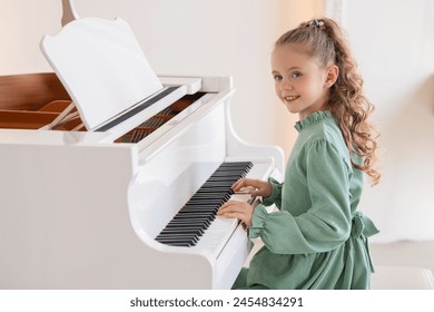 A young girl is playing the piano. She is wearing a green dress and has her hair in a ponytail - Powered by Shutterstock