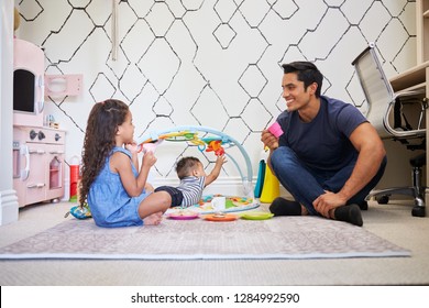 Young Girl Playing Tea Party With Dad, Sitting On The Floor, Baby Brother On A Play Mat Beside Them
