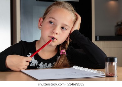 Young girl with ponytail daydreaming and holding her red pencil against her mouth while doing her homework. - Shutterstock ID 514692835
