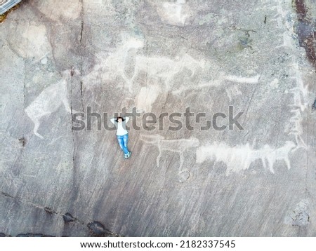 A young girl poses against the backdrop of primitive White Sea petroglyphs