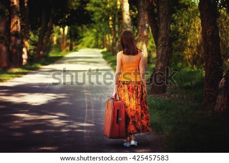 young girl posing on empty asphalt road with old vintage leather suitcase