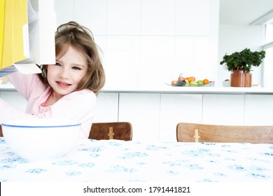 Young Girl Pouring Cereal From Box At Breakfast Table