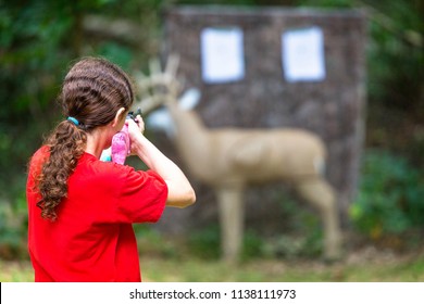 Young girl practcing target shooting with a bb gun at a model deer in the woods