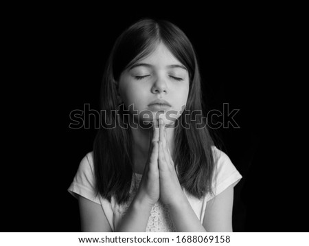 young girl prays, portrait on a dark background, black and white photo