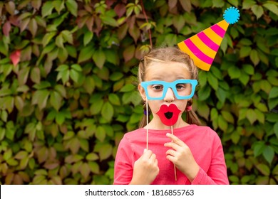 Young Girl Is Preparing For Birthday Party With Photo Booth Props. Photobooth Birthday And Party Set And Wedding.Happy Child With Glasses, Hat, Lips Props At Party Outdoor, On Leaves Background