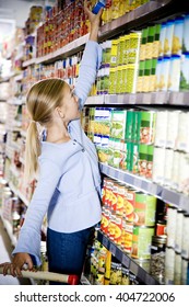 Young Girl Reaching Up To Get Something Off Of A Supermarket Shelf