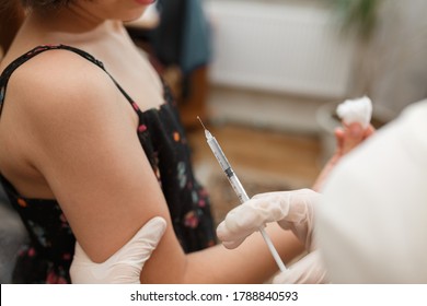 Young girl receiving vaccination immunisation by professional health worker, focus on shoulder. Medical syringe with vaccine. Health care and medicine concept.
