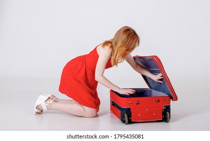A Young Girl In A Red Dress Looks Into An Open Suitcase And Puts Things Together