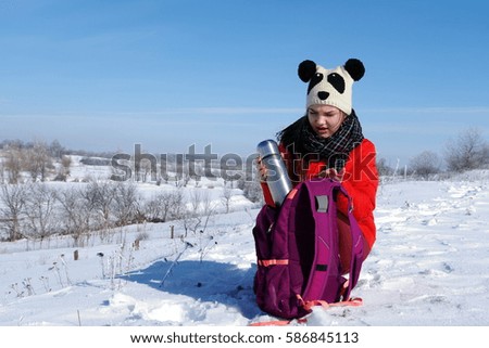 A young girl in a red jacket drinking tea on a background of a winter landscape